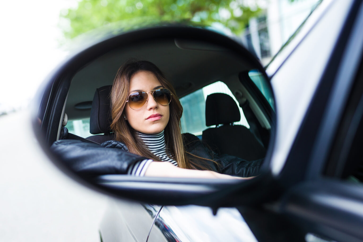 Woman wearing sunglasses while driving, reflected in a car side mirror