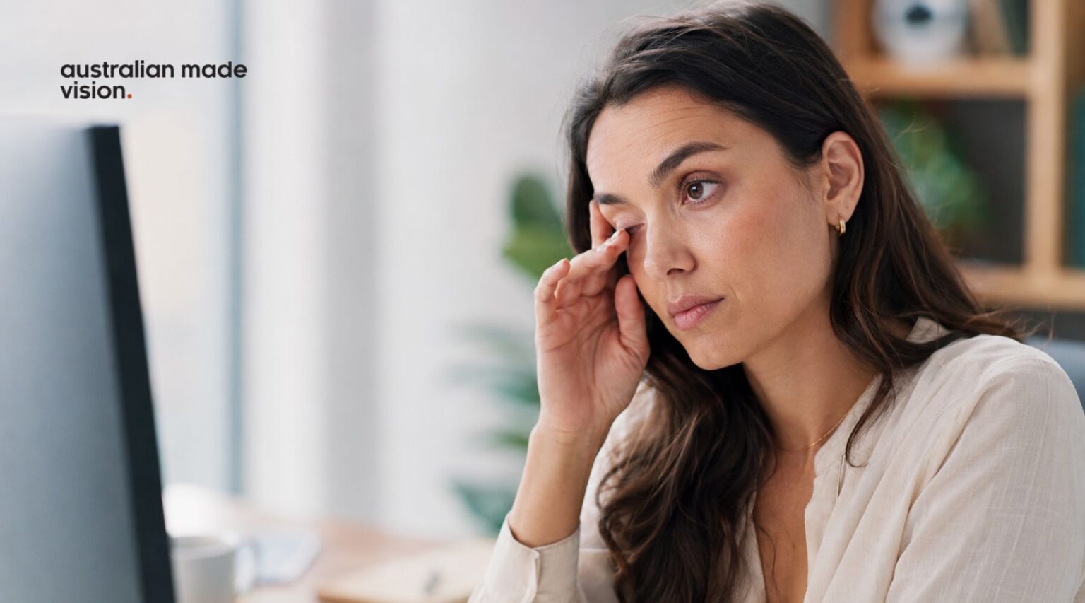 Woman rubbing an irritated eye while using a computer, illustrating possible dry eye syndrome symptoms